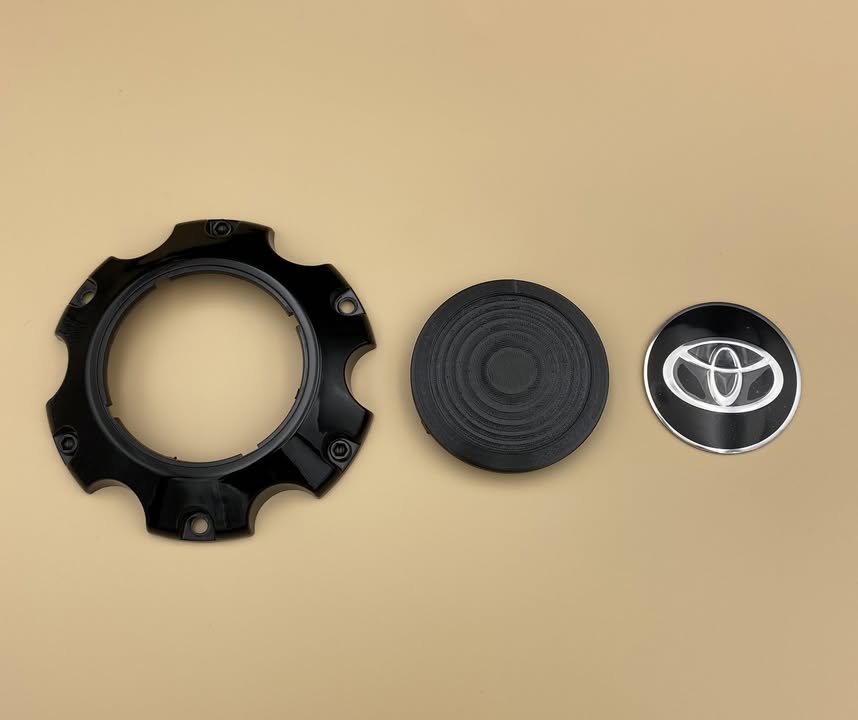 The three parts laid out: the outer cap ring, the 3D printed adapter disc, and the Toyota emblem